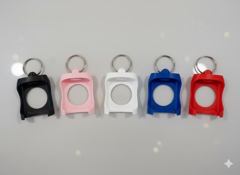 May include: Five colorful keychains in black, pink, white, blue, and red. Each keychain has a circular opening and a silver metal ring at the top for attaching keys. The keychains are made of a smooth, solid material.