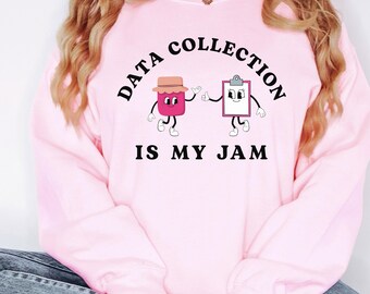 May include: Pale pink sweatshirt with the slogan "DATA COLLECTION IS MY JAM" in a curved black font. The design includes cartoon images of a jam jar and a clipboard, both with arms and legs, waving.