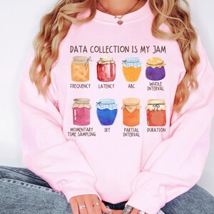 Może przedstawiać: Różowa bluza z napisem "DATA COLLECTION IS MY JAM" i ilustracjami słoików z dżemem oznaczonych różnymi metodami gromadzenia danych, takimi jak "Częstotliwość", "Opóźnienie", "ABC", "Cały przedział", "Momentalne pobieranie próbek", "IRT", "Częściowy przedział" i "Czas trwania".