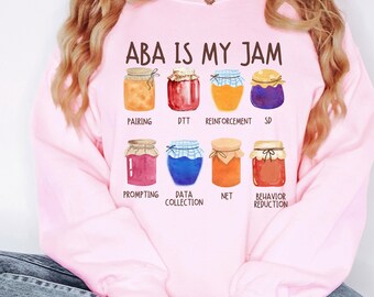 May include: A pale pink sweatshirt featuring the phrase "ABA IS MY JAM" and illustrations of eight jam jars. Each jar is a different colour and labelled with terms such as "Pairing", "DTT", and "Reinforcement".