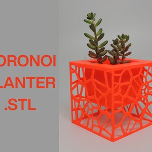 May include: Bright orange Voronoi planter with a geometric design, holding a small succulent plant. The planter is cube-shaped and features the text "VORONOI PLANTER .STL" in orange. The plant has green and brown leaves.