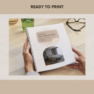 May include: A spiral-bound welcome packet for tenants, held open to display the cover and a bedroom image. The cover reads "Tenant Welcome Packet" with additional text. The background is a light wood surface.