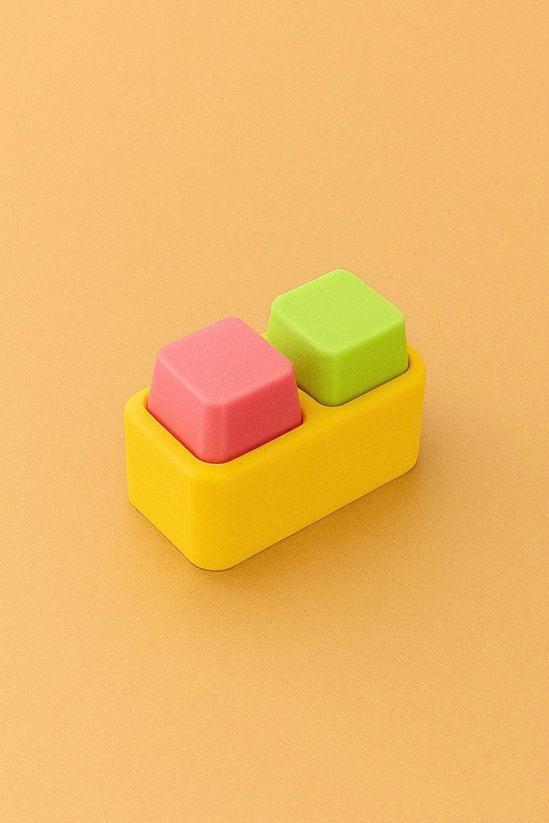 May include: A yellow rectangular container holds two square objects. One is pink, the other is green. The background is a solid orange color. The objects appear to be made of a soft material.