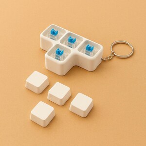May include: A white keyboard switch tester with five blue switches and keycaps, attached to a keychain. Six additional white keycaps are scattered nearby. The background is a solid, light orange color.