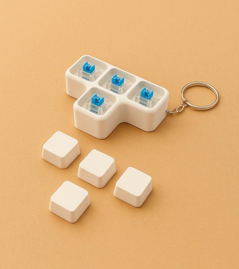 May include: A white keyboard switch tester with five blue switches and keycaps, attached to a keychain. Six additional white keycaps are scattered nearby. The background is a solid, light orange color.