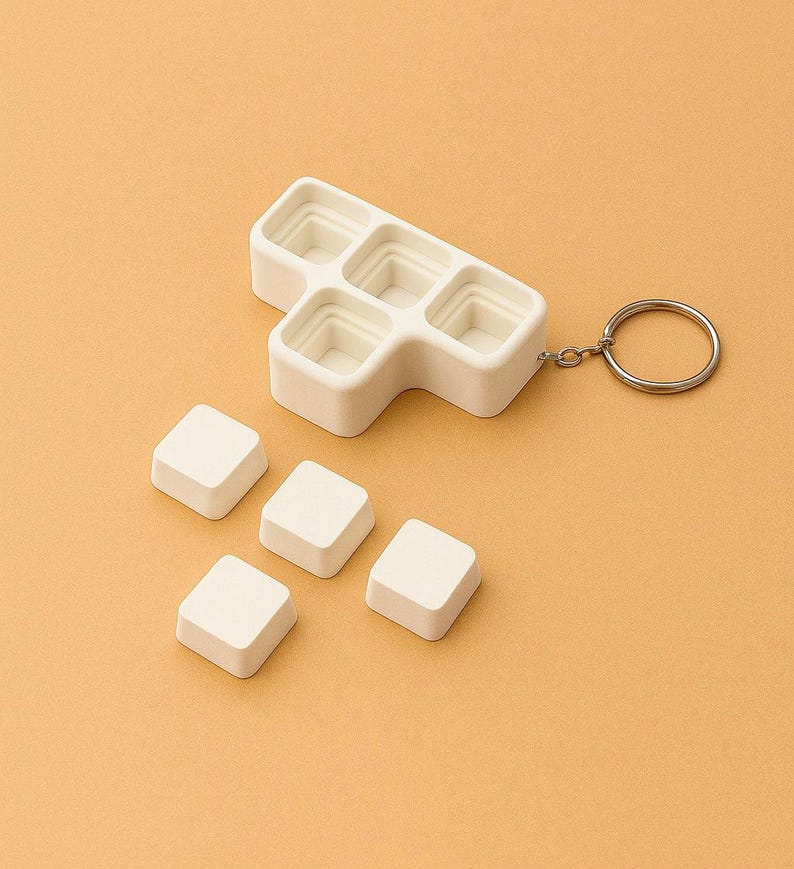 May include: A white, geometric-shaped keychain with a silver ring. The keychain has a series of square compartments, with five detached square pieces. The items are set against a solid, light orange background.