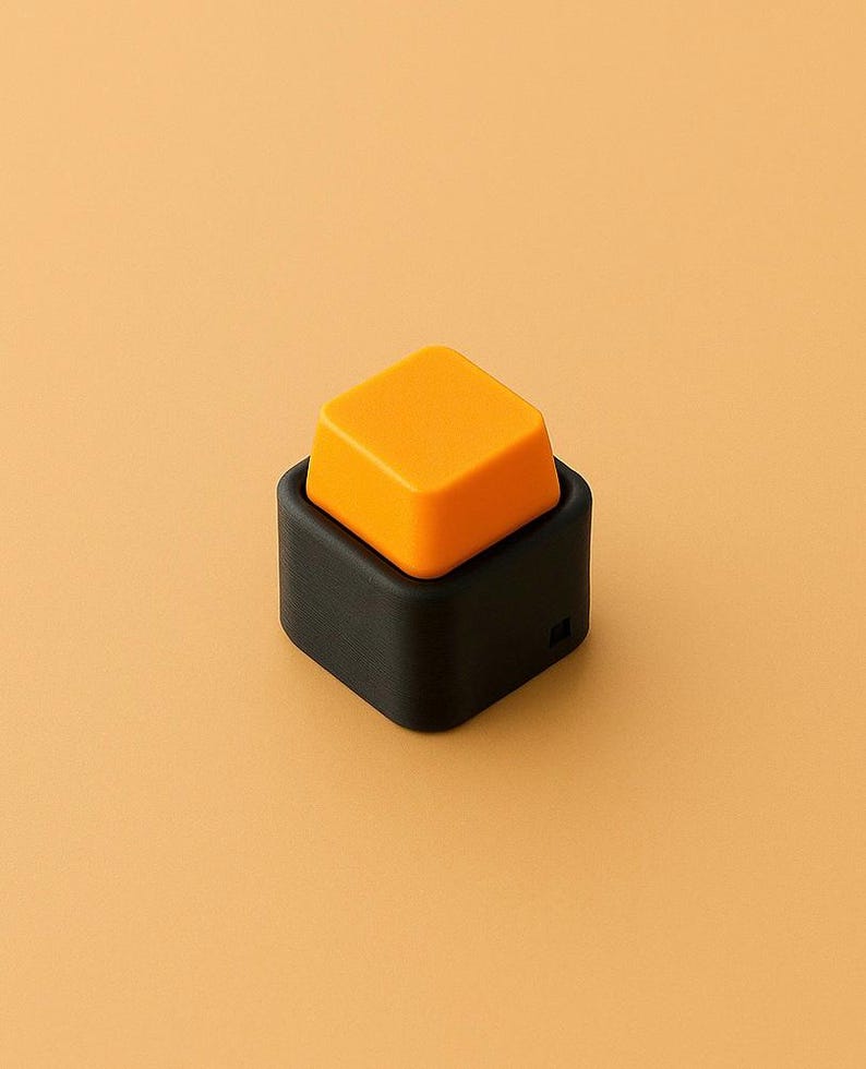 May include: A modern, minimalist design featuring a black square base with an orange square button on top. The button is slightly raised, creating a 3D effect. The background is a solid, warm orange.