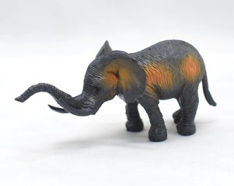 Puede incluir: Figura de elefante de juguete gris y naranja. El elefante tiene una trompa curvada, orejas grandes y está de pie sobre cuatro patas. El juguete está sobre un fondo blanco.