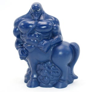 May include: A dark blue figurine of a centaur with a muscular human upper body and a horse-like lower body. The figurine has a detailed design, with defined muscles and a textured surface. The centaur is standing upright on a white background.