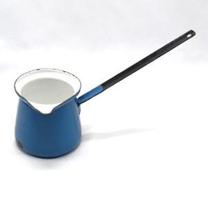 Peut inclure: Une cafetière en émail bleu avec une longue poignée noire. La cafetière a un intérieur blanc et un bec verseur. La poignée est fixée à la cafetière avec une section bleue. La cafetière est probablement vintage.