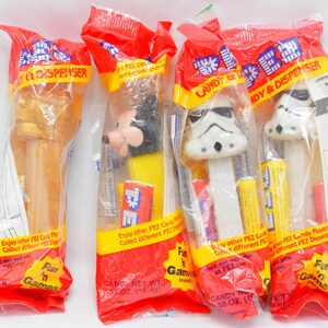 Könnte beinhalten: Vier versiegelte PEZ-Bonbonspender in roter Verpackung. Die Spender zeigen Charaktere wie Micky Maus und Sturmtruppen. Die Verpackung enthält den Text "Candy & Dispenser" und "Fun 'n Games".