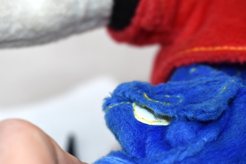 K&ouml;nnte beinhalten: Nahaufnahme eines Pl&uuml;schtiers in Blau, Rot und Wei&szlig;. Der blaue Teil hat gelbe N&auml;hte. Das Spielzeug hat eine weiche, flauschige Textur. Das Bild ist vor einem schlichten wei&szlig;en Hintergrund aufgenommen.