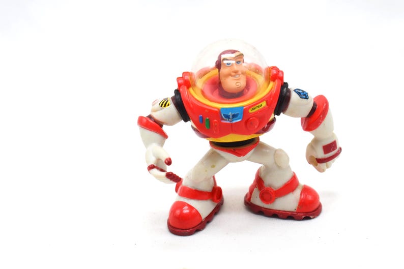 May include: A Buzz Lightyear action figure from the Toy Story franchise. The figure is primarily white with red and yellow accents. It features a clear helmet, a red chest plate, and red boots. The figure is in a crouching pose.