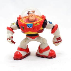 May include: A Buzz Lightyear action figure, featuring a red, white, and yellow spacesuit with a clear helmet. The toy has articulated limbs and is posed in a standing position. The figure is a collectible item.