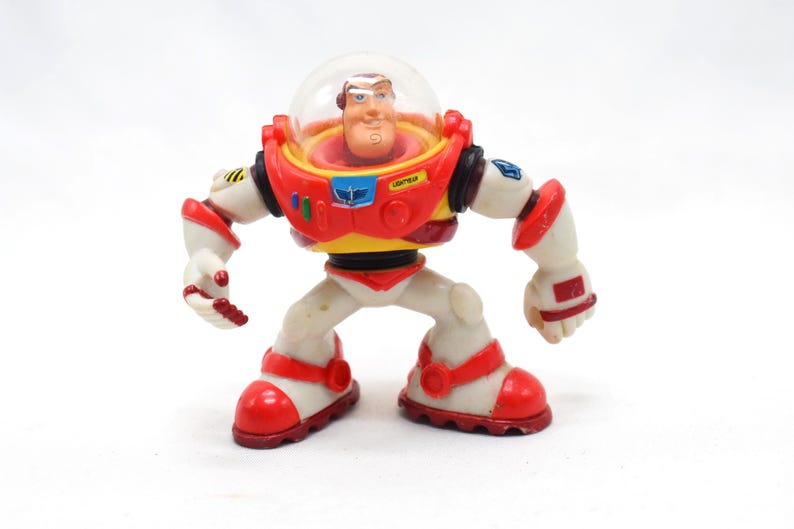 May include: A Buzz Lightyear action figure, featuring a red, white, and yellow spacesuit with a clear helmet. The toy has articulated limbs and is posed in a standing position. The figure is a collectible item.