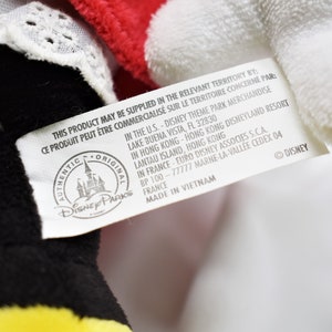 K&ouml;nnte beinhalten: Ein wei&szlig;es Etikett mit schwarzem Text, das an einem schwarzen und gelben Pl&uuml;schtier befestigt ist. Das Etikett lautet "This product may be supplied in the relevant territory by:  Ce produit peut &ecirc;tre commercialis&eacute; sur le territoire concern&eacute; par:  Authentic Original Disney Parks  In the U.S. - Disney Theme Park Merchandise Lake Buena Vista, FL 32830  In Hong Kong - Hong Kong Disneyland Resort Lantau Island, Hong Kong  In France - Euro Disney Associes S.C.A. BP 100 - 77777 Marne-la-Vall&eacute;e Cedex 04 France  Made in Vietnam  &copy; Disney"
