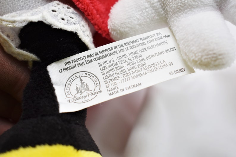 K&ouml;nnte beinhalten: Ein wei&szlig;es Etikett mit schwarzem Text, das an einem schwarzen und gelben Pl&uuml;schtier befestigt ist. Das Etikett lautet "This product may be supplied in the relevant territory by:  Ce produit peut &ecirc;tre commercialis&eacute; sur le territoire concern&eacute; par:  Authentic Original Disney Parks  In the U.S. - Disney Theme Park Merchandise Lake Buena Vista, FL 32830  In Hong Kong - Hong Kong Disneyland Resort Lantau Island, Hong Kong  In France - Euro Disney Associes S.C.A. BP 100 - 77777 Marne-la-Vall&eacute;e Cedex 04 France  Made in Vietnam  &copy; Disney"