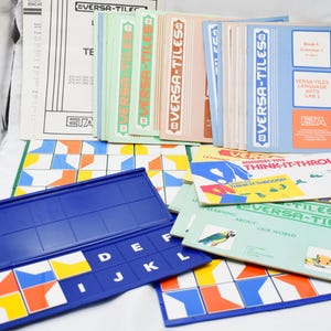 May include: A collection of educational Versa-Tiles learning materials. The image shows various colorful tiles, booklets, and a blue tile holder. The booklets have titles like "Think-It-Through" and "Learning About Our World."