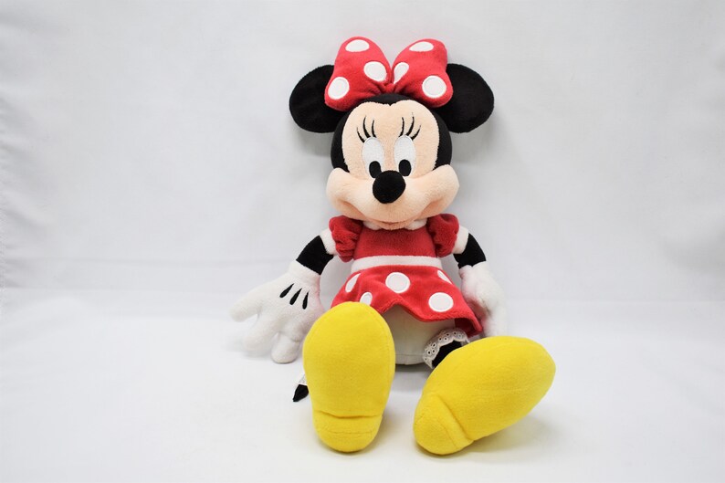 K&ouml;nnte beinhalten: Ein Pl&uuml;schtier von Minnie Mouse, die ein rotes Kleid mit wei&szlig;en Punkten und eine rote Schleife mit wei&szlig;en Punkten tr&auml;gt. Sie hat schwarze Augen, eine schwarze Nase und gelbe Schuhe.