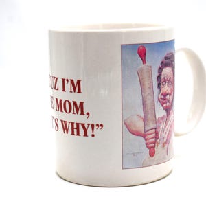 Op de afbeelding: Witte keramische mok met een handvat. De mok heeft rode tekst met de tekst "CUZ I'M THE MOM, THAT'S WHY!" en een cartoonillustratie van een vrouw die een deegroller vasthoudt.