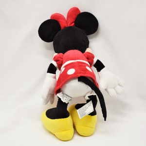 K&ouml;nnte beinhalten: Ein Pl&uuml;schtier von Minnie Mouse, das ein rotes Kleid mit wei&szlig;en Punkten und gelbe Schuhe tr&auml;gt. Das Spielzeug hat schwarze Ohren und eine rote Schleife.