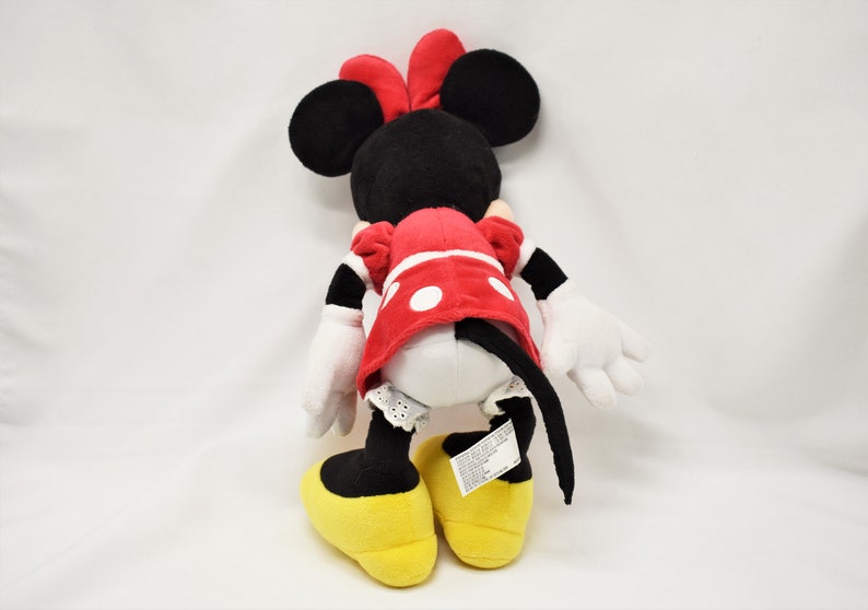K&ouml;nnte beinhalten: Ein Pl&uuml;schtier von Minnie Mouse, das ein rotes Kleid mit wei&szlig;en Punkten und gelbe Schuhe tr&auml;gt. Das Spielzeug hat schwarze Ohren und eine rote Schleife.
