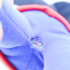 May include: Close-up of a torn blue plush toy with red and black accents. The tear reveals the inner stuffing of the toy. A hand is partially visible in the image.