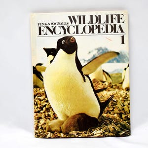 以下が含まれることがあります： 「Wildlife Encyclopedia」Volume 1と題された、ヴィンテージのハードカバー本。表紙には、自然の生息地でのペンギンの写真が掲載されています。本のタイトルは、白い背景に太字の黒い文字で書かれています。