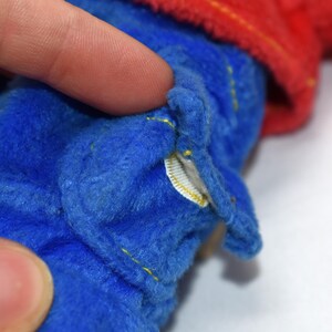 K&ouml;nnte beinhalten: Nahaufnahme eines blauen Pl&uuml;schtiers mit gelben N&auml;hten und einem roten Stoffdetail. Der Stoff des Spielzeugs ist weich und strukturiert. Ein kleines wei&szlig;es Etikett ist sichtbar.