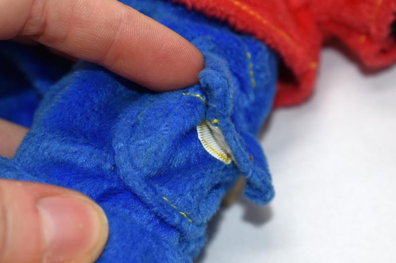 K&ouml;nnte beinhalten: Nahaufnahme eines blauen Pl&uuml;schtiers mit gelben N&auml;hten und einem roten Stoffdetail. Der Stoff des Spielzeugs ist weich und strukturiert. Ein kleines wei&szlig;es Etikett ist sichtbar.