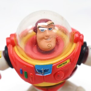 May include: A Buzz Lightyear action figure, featuring a red, yellow, and white spacesuit with a clear helmet. The figure has a smiling face and the word "LIGHTYEAR" is visible on the chest. A classic toy.