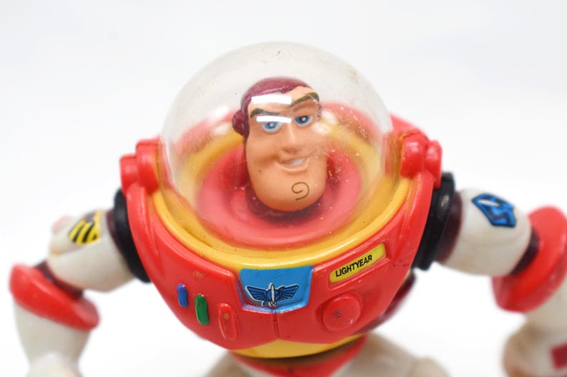 May include: A Buzz Lightyear action figure, featuring a red, yellow, and white spacesuit with a clear helmet. The figure has a smiling face and the word "LIGHTYEAR" is visible on the chest. A classic toy.