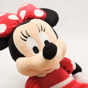 K&ouml;nnte beinhalten: Ein Pl&uuml;schtier von Minnie Mouse, die ein rotes Kleid mit wei&szlig;en Punkten und eine rote Schleife mit wei&szlig;en Punkten tr&auml;gt.