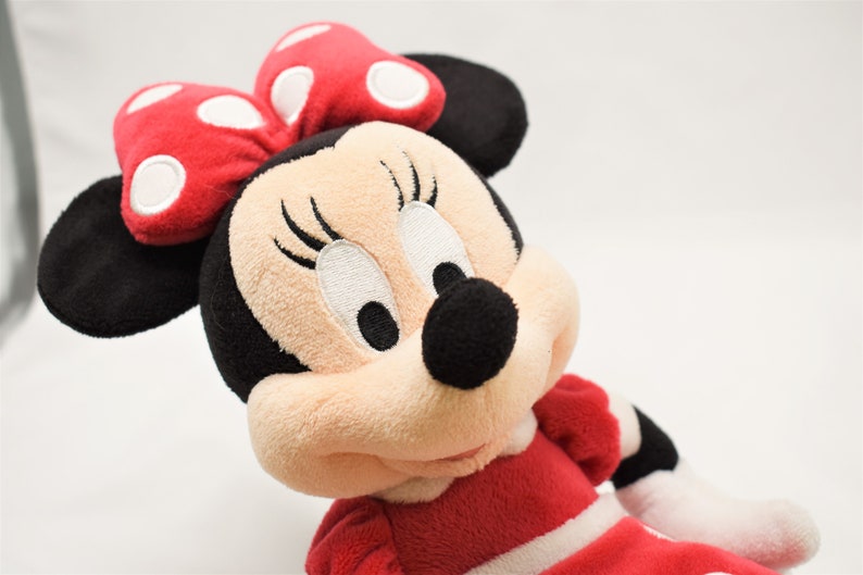 K&ouml;nnte beinhalten: Ein Pl&uuml;schtier von Minnie Mouse, die ein rotes Kleid mit wei&szlig;en Punkten und eine rote Schleife mit wei&szlig;en Punkten tr&auml;gt.