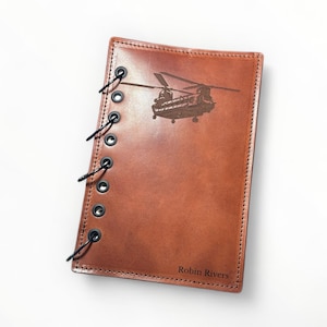 May include: A brown leather journal with a black spiral binding. The cover features an engraved image of a helicopter and the text "Robin Rivers".