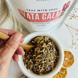 Loose leaf herbal tea in white pouch labeled Vata blend with cup of warm tea, calming herbal tea for cozy self care rituals, caffeine free loose leaf tea