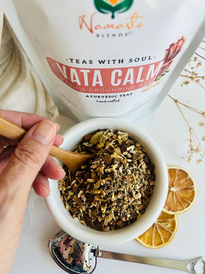 Loose leaf herbal tea in white pouch labeled Vata blend with cup of warm tea, calming herbal tea for cozy self care rituals, caffeine free loose leaf tea