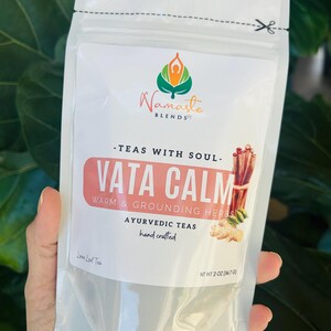 Loose leaf herbal tea in white pouch labeled Vata blend with cup of warm tea, calming herbal tea for cozy self care rituals, caffeine free loose leaf tea