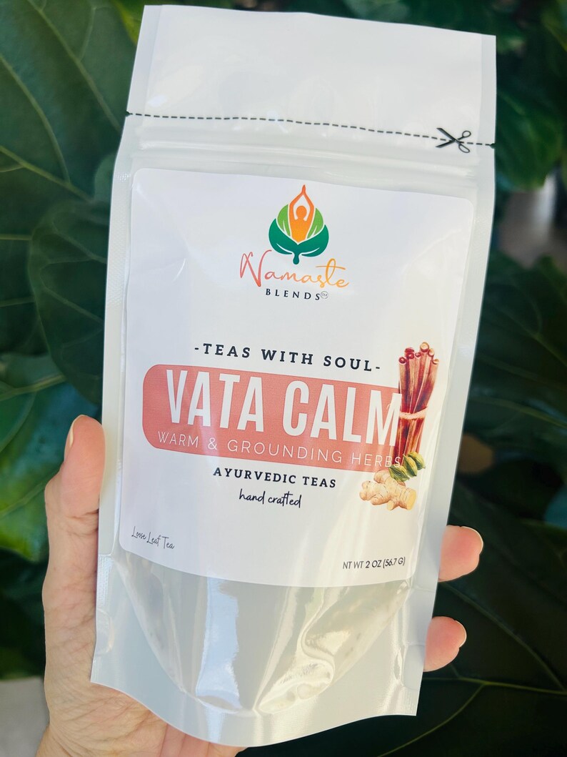 Loose leaf herbal tea in white pouch labeled Vata blend with cup of warm tea, calming herbal tea for cozy self care rituals, caffeine free loose leaf tea