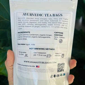 Loose leaf herbal tea in white pouch labeled Vata blend with cup of warm tea, calming herbal tea for cozy self care rituals, caffeine free loose leaf tea