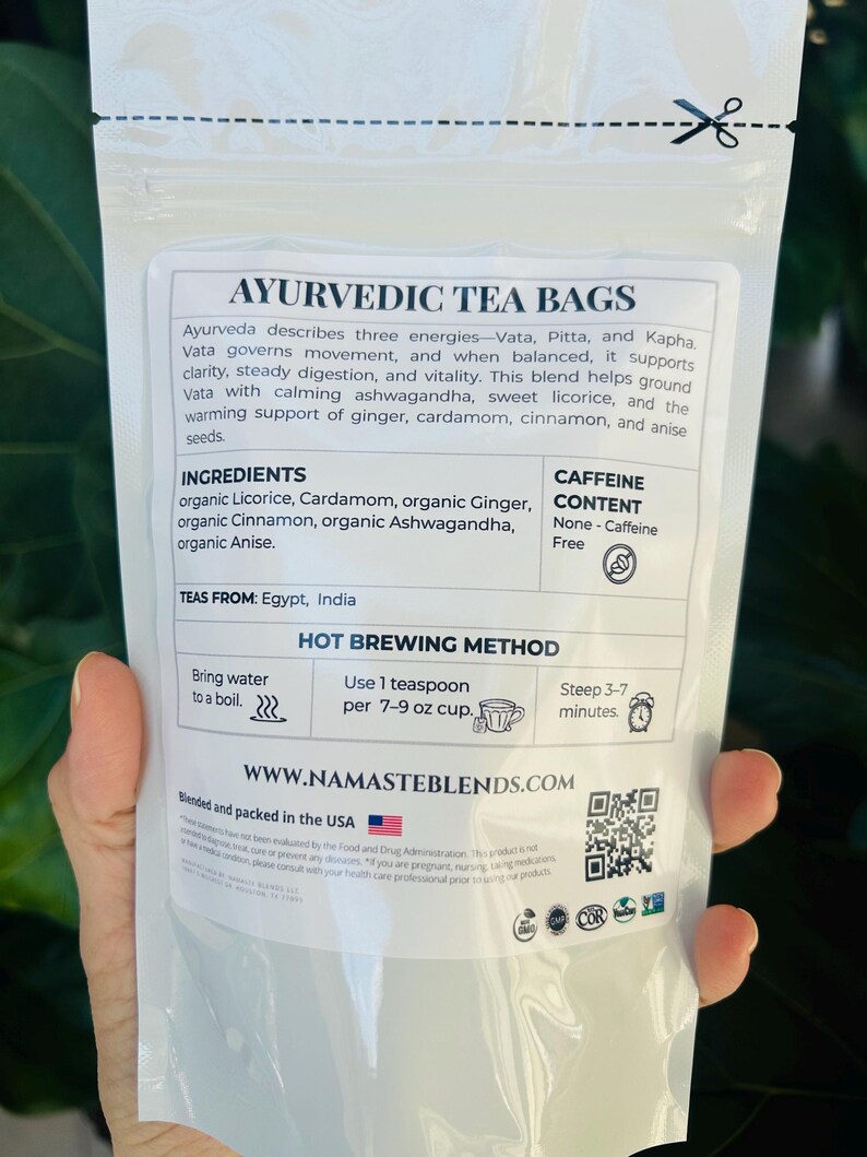 Loose leaf herbal tea in white pouch labeled Vata blend with cup of warm tea, calming herbal tea for cozy self care rituals, caffeine free loose leaf tea
