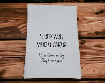 May include: White tea towel with black text that reads "Sleep well middle finger. You have a big day tomorrow."