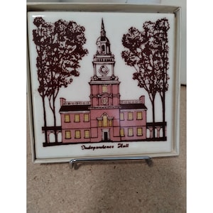 May include: A white ceramic tile with a brown and pink illustration of Independence Hall in Philadelphia, Pennsylvania. The tile has the text "Independence Hall" printed below the illustration.