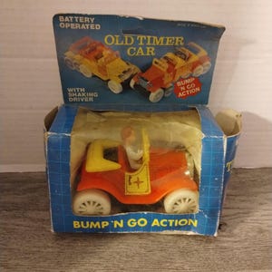 May include: A red and yellow toy car with a bump and go action. The car has a shaking driver and is battery operated. The box says "Old Timer Car".