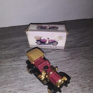 May include: A small, red and black toy car with a tan top. The car is in a box with the word "Victoria" printed on it.