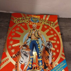 May include: A red and gold program cover for Ringling Bros. and Barnum & Bailey Circus. The cover features a man in a blue and gold costume standing between two tigers. The text on the cover reads "Ringling Bros. and Barnum & Bailey Circus, The Greatest Show on Earth".