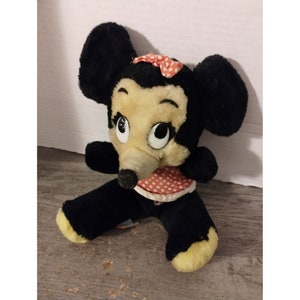 Puede incluir: Un juguete de peluche vintage de Minnie Mouse, con pelaje negro, un vestido de lunares rojos y blancos y un lazo rojo con lunares blancos.