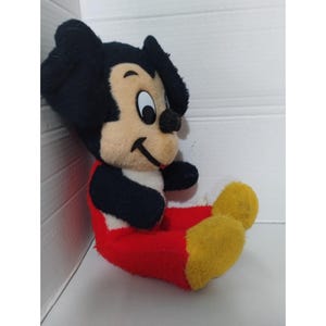 May include: A vintage plush Mickey Mouse toy with black ears, a black and white face, and red and yellow pants.