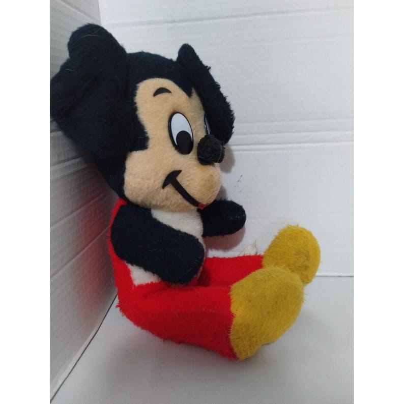 May include: A vintage plush Mickey Mouse toy with black ears, a black and white face, and red and yellow pants.