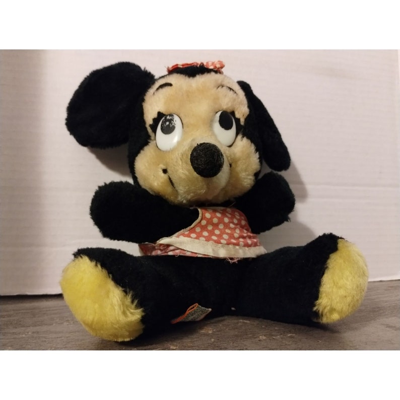 Puede incluir: Un juguete de peluche vintage de Minnie Mouse con un vestido de lunares rojos y blancos. El juguete tiene pelo negro, pies amarillos y grandes ojos negros.